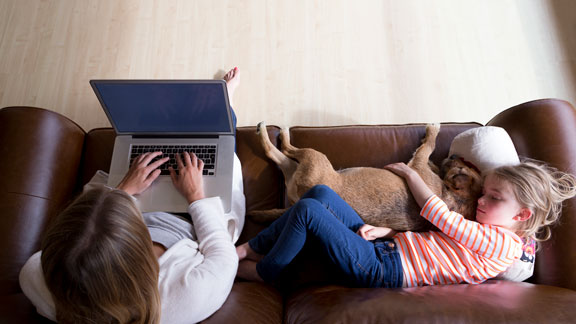 female with laptop on couch with kid and dog